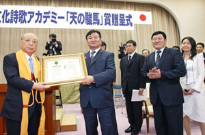 Dr. G. Mend-Ooyo (center) presents the certificate of commendation to Mr. Ikeda (left). Mr. Tsend Batsaikhan and Ms. Munkhazaya Mend-Ooyo are standing to Dr. Mend-Ooyo's right (foreground).